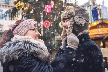 Karlı bir kış günü, Noel pazarında birbirlerine gülümseyen bir çift.