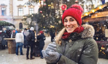 Kış zamanı Almanya 'da bir Noel pazarında kar taneleriyle kırmızı bereli ve eşarplı gülümseyen bir kadın..
