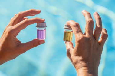 Bir otelin kaplıca merkezinde havuz suyu pH testi için pembe ve sarı sıvılı şişeleri tutan eller.