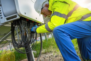 Güneş paneli parkındaki bir dağıtım istasyonunda kabloları kontrol eden bir mühendis. Alternatif enerji ekolojik konsept görüntüsü.
