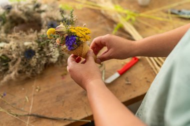 Bir konide, ahşap bir masanın üzerinde küçük bir buket kurutulmuş çiçek hazırlayan eller.
