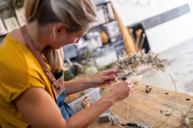 İyi aydınlatılmış bir atölyede çiçeklere iplik takan odaklanmış kadın çiçekçi.