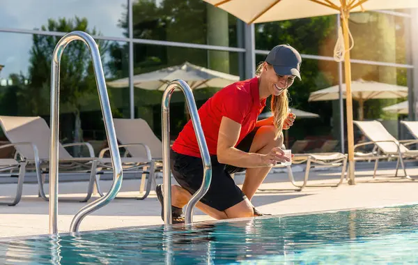 Service worker at a pool takes a water sample for PH analysis of the water quality in a hotel