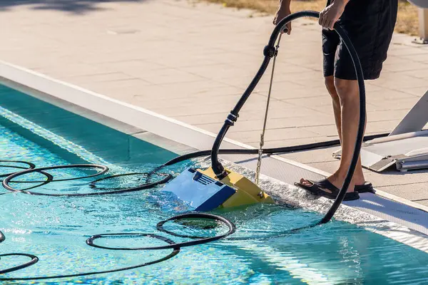 Person operating a pool vacuum cleaner at the side of a swimming pool