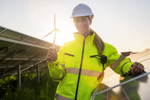 Renewable energy technician holding a wind turbine model at solar farm. Alternative energy ecological concept image.