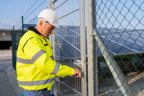 Electrical engineer in safety gear opening a gate to a solar field