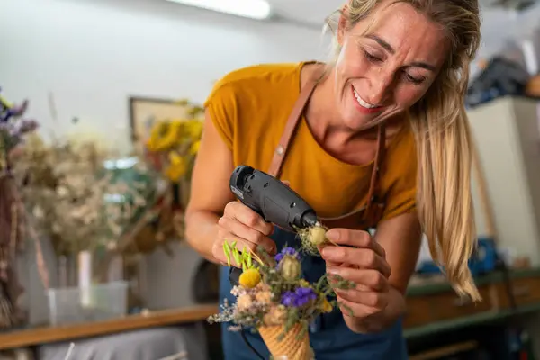 Smiling female florist using a glue gun on a floral ice cream cone arrangement