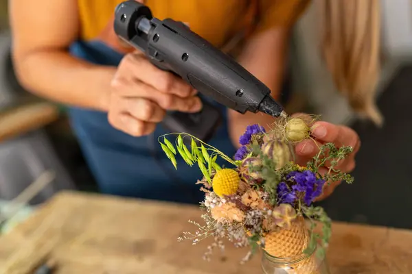 Close-up of hands using a glue gun to assemble a floral arrangement in a cone