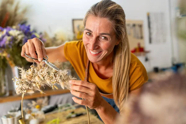 smiling florist woman trims a delicate dried flower arrangement, working meticulously in a studio filled with floral elements