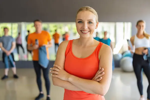 Confident woman in orange tank top standing with arms crossed in a gym. Teamwork Concept image