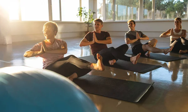Yoga class performing seated twist poses, sunlit room, group of adults