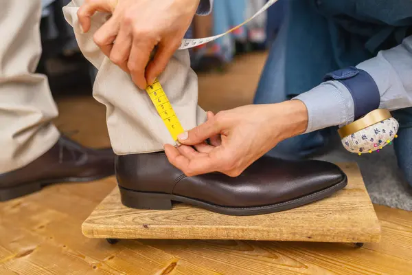 茶色の靴の上の人の足首のテープが付いているズボンの長さを測定して下さい ストック写真