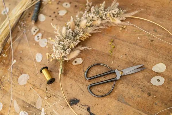 散らされた花びらおよび糸のスプールが付いている木のテーブルの乾燥された花の配置そしてハサミ ロイヤリティフリーのストック画像