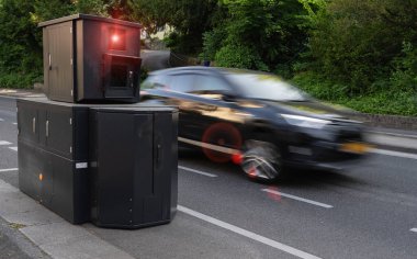 Speed enforcement camera on roadside with a car in high speed motion blur, foliage background clipart