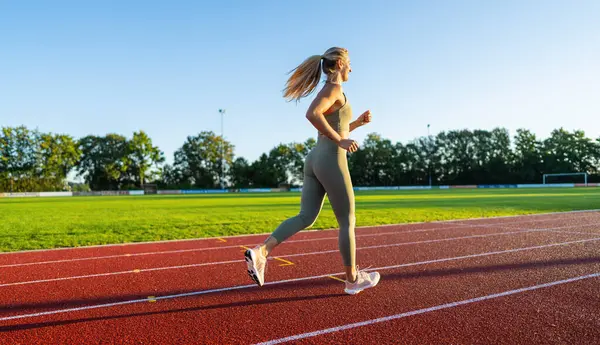 stock image Side view of a woman running on a track in the sunlight
