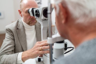 Optometrist yaşlı bir hastanın gözlerini incelemek için özel ekipman kesici lamba kullanıyor..