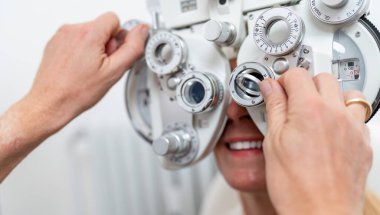 Close-up of a optician adjusting a phoropter for a female patient during an eye test at the ophthalmology clinic. Healthcare and medicine concept clipart