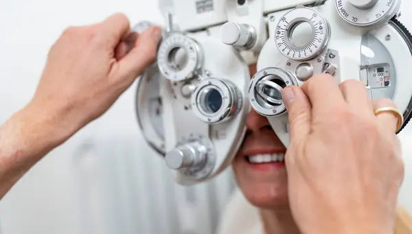 stock image Close-up of a optician adjusting a phoropter for a female patient during an eye test at the ophthalmology clinic. Healthcare and medicine concept