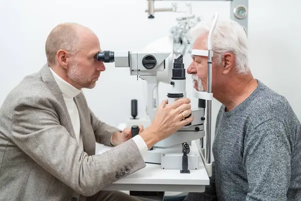 Optometrista Examinando Los Ojos Paciente Masculino Mayor Usando Una Lámpara Imagen De Stock