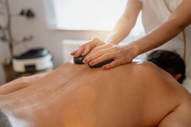 Terapist, müşterisine sıcak taş masajı yapıyor.