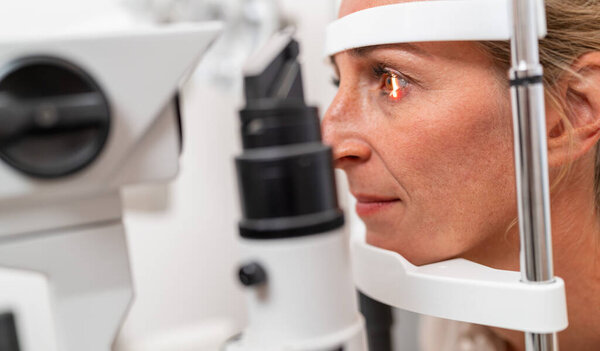 Woman undergoing an eye examination with a focus on her illuminated eye using a slit lamp at the ophthalmology clinic. Close-up photo. Healthcare and medicine concept