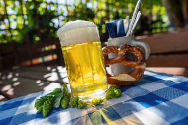 Beer mug with fresh pretzel or brezen and hops at Biergarten or Oktoberfest, Munich, Germany clipart