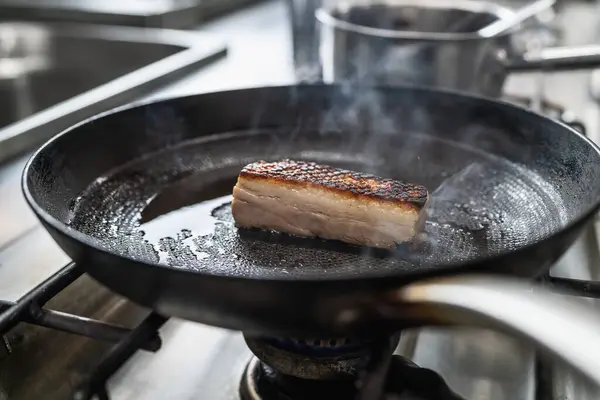 Crispy pork belly Roast in hot pan with oil at a gas stove in a professional kitchen at a restaurant. Luxury hotel cooking concept image.