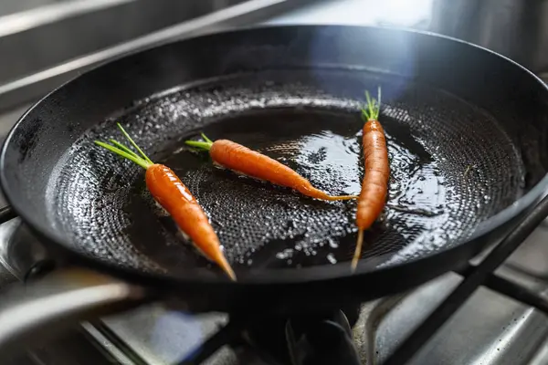 Fresh carrots frying in oiled pan at a gas stove in a professional kitchen at a restaurant. Luxury hotel cooking concept image.