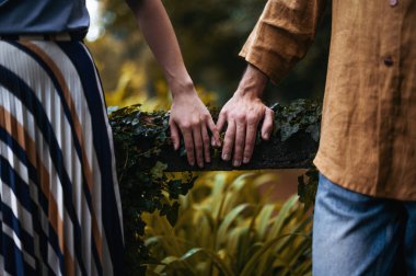 Genç çiftlerin güzel bir sonbahar parkında el ele tutuştukları romantik bir fotoğraf. Birbirlerine yakın çekimde makarada dinlenirken gösteriliyor. Çiftlerin elleri renkli yapraklarla çevrili.