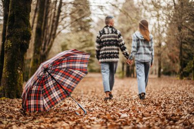 A romantic photo of a young couple walking hand in hand away from the camera on a beautiful landscape. They both have big smiles on their faces as they walk together, capturing the essence of their
