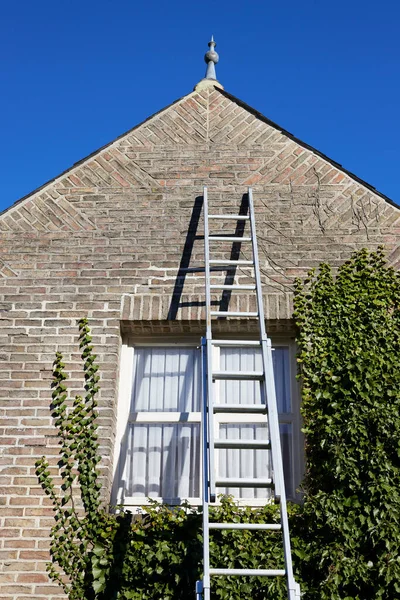 stock image Ladder stands against yellow brick house wall near window