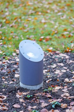 Modern metal projektörlü fotoğraf bir çimenlik alana yerleştirilmiş dairesel şekillerin açık havada kullanılması için ışık saçar.