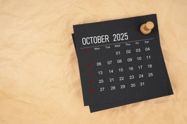 Kahverengi kağıt üzerinde raptiye ile Ekim 2025 için siyah takvim sayfası.