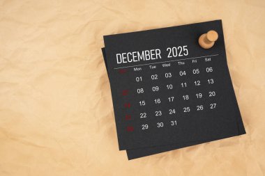 Kahverengi kağıt üzerinde raptiye ile Aralık 2025 siyah takvim sayfası.