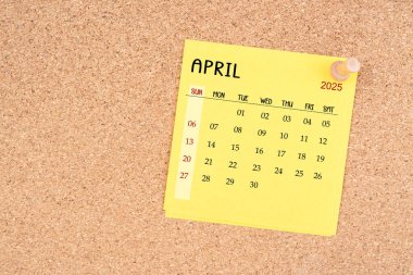 Yellow calendar sheet for April 2025 with thumbtack on wooden board. clipart