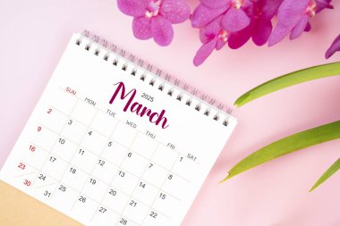 Mart 2025 'te çiçek açan pembe orkideli masa takvimi. Düz yatıyordu.