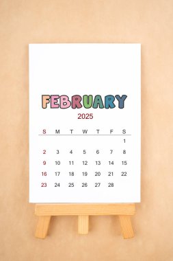 Şubat 2025 takvim sayfası eski kahverengi arka planda ahşap sehpa ile.