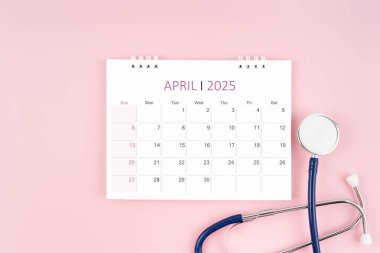 Nisan 2025 masa takvimi ve pembe arka plan steteskop, Tıbbi randevu kavramı.