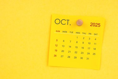 Sarı arkaplanda raptiyesi olan Ekim 2025 takvim sayfası.