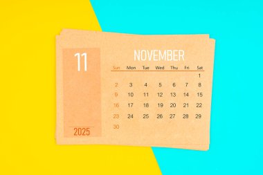 Sarı ve mavi arka planda 2025 Kasım ayı için kahverengi takvim kartı.