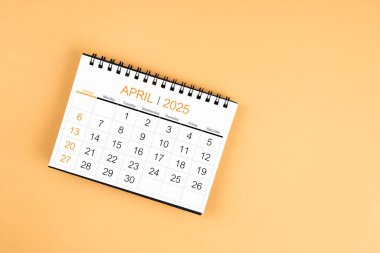 Sarı pastel arka planda Nisan 2025 masa takviminin üst görünümü.