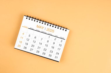 Sarı pastel arka planda Mayıs 2025 masa takviminin üst görünümü.