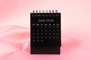 Pembe ipek tekstil arka planında Haziran 2026 için siyah masa takvimi.