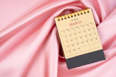 Mart 2026 Pembe ipek tekstil arkaplan üzerine kahverengi kağıt masa takvimi.