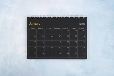 Ocak 2026 için boş takvim, mavi ahşap zemin üzerinde siyah spiral masaüstü takvimi.