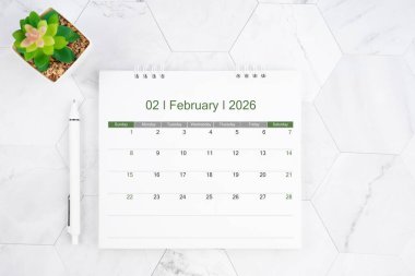 Masa takvimi Şubat 2026 'da beyaz mermer arka planda kalemle.
