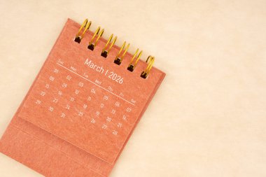 Mart 2026 için küçük kırmızı masa takvimi eski kahverengi kağıt arka planda.