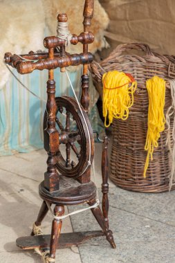 Doğal boyalarla boyanmış yünlü bir açık hava dükkanının dikey görüntüsü ve ön planda antik bir pedal çevirme çarkı.