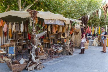 ALCALA DE HENARES, MADRID, SPAIN - OCTOBER 10, 2016:  t tourists looking at an outdoor shop of wools dyed with natural dyes and several pedal wooden spinning wheels. taken during the celebration of a medieval festival in the streets of the city