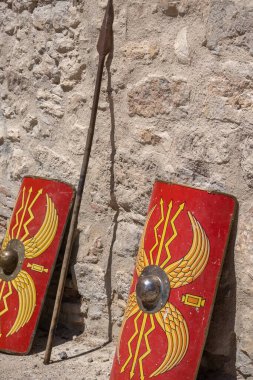 İki kırmızı kalkanın dikey görüntüsü ve antik Roma lejyonlarından bir askerin mızrağı.